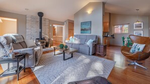 A spacious living room with a fireplace, a grey sofa, a brown armchair, and a dining area with wooden cabinets. - Relax in Kings Beach Canterbury Pines- 3BR with Hot tub! (Kings Beach)