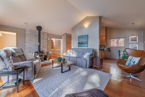 A spacious living room with a fireplace, a grey sofa, a brown armchair, and a dining area with wooden cabinets. - Relax in Kings Beach Canterbury Pines- 3BR with Hot tub! (Kings Beach)