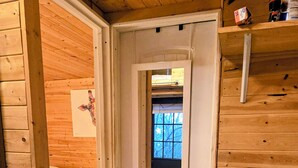 Una stanza tipo baita in legno con un letto, una piccola finestra e un angolo cottura con lavello.