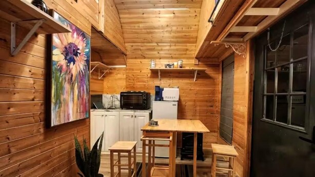 Un accogliente chalet in legno con angolo cottura, zona pranzo con sgabelli e una grande finestra.