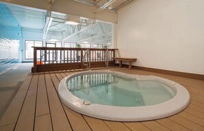 Ein Whirlpool in einem großzügigen Innenbereich mit Holzterrasse, einer Holzbank und einem Geländer.