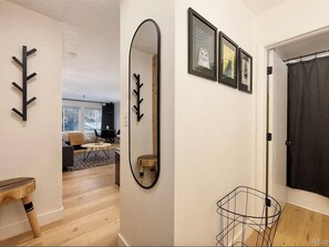 A hallway with a mirror, a coat rack, and a door with a black curtain. - Hip Ski Pad • Hot Tub • Steps to Downtown (Winter Park)