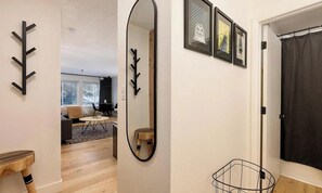 Ein modernes Interieur mit Holzboden, einem Spiegel, einem schwarzen Kleiderständer und gerahmten Kunstwerken an der Wand.