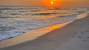 Una playa con un atardecer, olas y huellas en la arena.