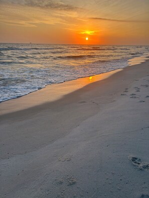 Ein Strand bei Sonnenuntergang, mit Wellen und Fußspuren im Sand.