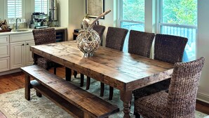 Un comedor con una mesa de madera, sillas de mimbre, un banco y una lámpara colgante.