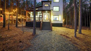 A modern two-story cabin with a stone facade, wooden deck, and a staircase leading to the entrance. - New Luxury! Starlight Pines Hot Tub-Arcade-Firepit (Broken Bow)