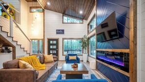 A modern living room with a staircase, a large TV wall, and a cozy seating area. - New Luxury! Starlight Pines Hot Tub-Arcade-Firepit (Broken Bow)