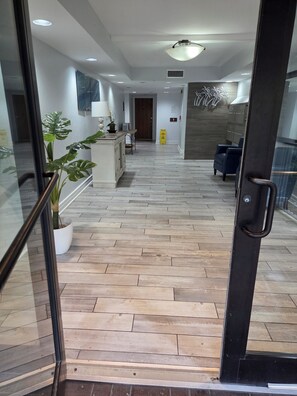 Eine Hotelhalle mit Holzboden, einer Rezeption, einer Sitzecke und einer Tür zu einem weiteren Raum.
