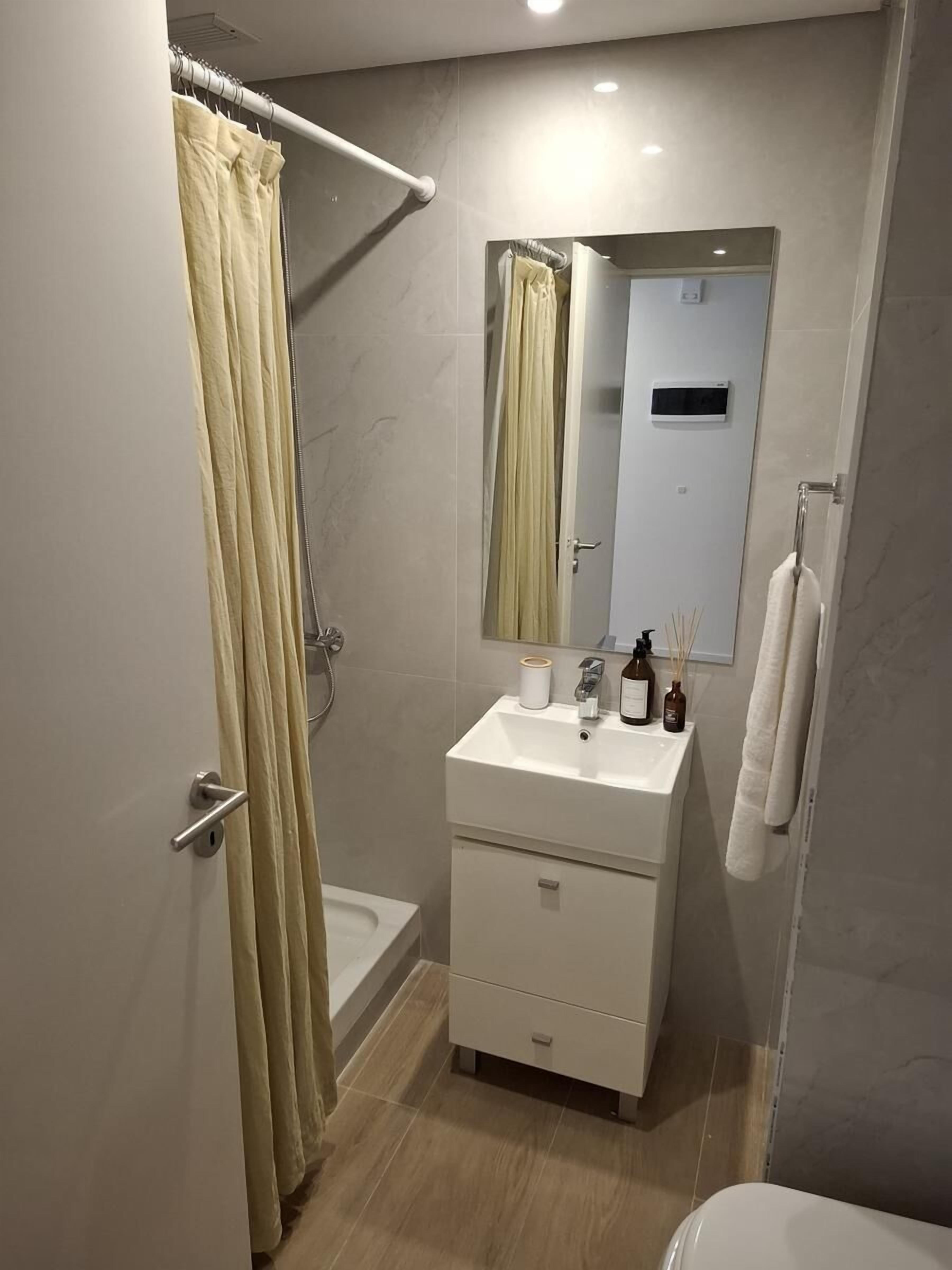 Un baño moderno con ducha, lavamanos con espejo y un inodoro.