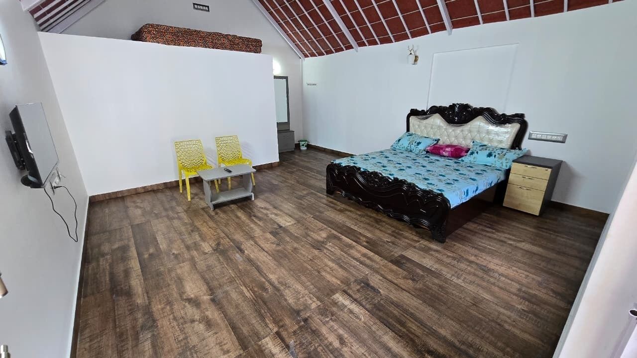 A bedroom with a wooden floor, a bed with a black headboard, two chairs, a bedside table, and a small cabinet.