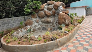 Un jardín ajardinado con muro de piedra, un pequeño elemento acuático y diversas plantas.