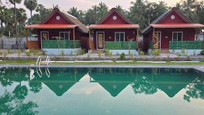 Una piscina con tres cabañas de techo rojo, cada una con una puerta y una ventana, y una valla verde al frente.