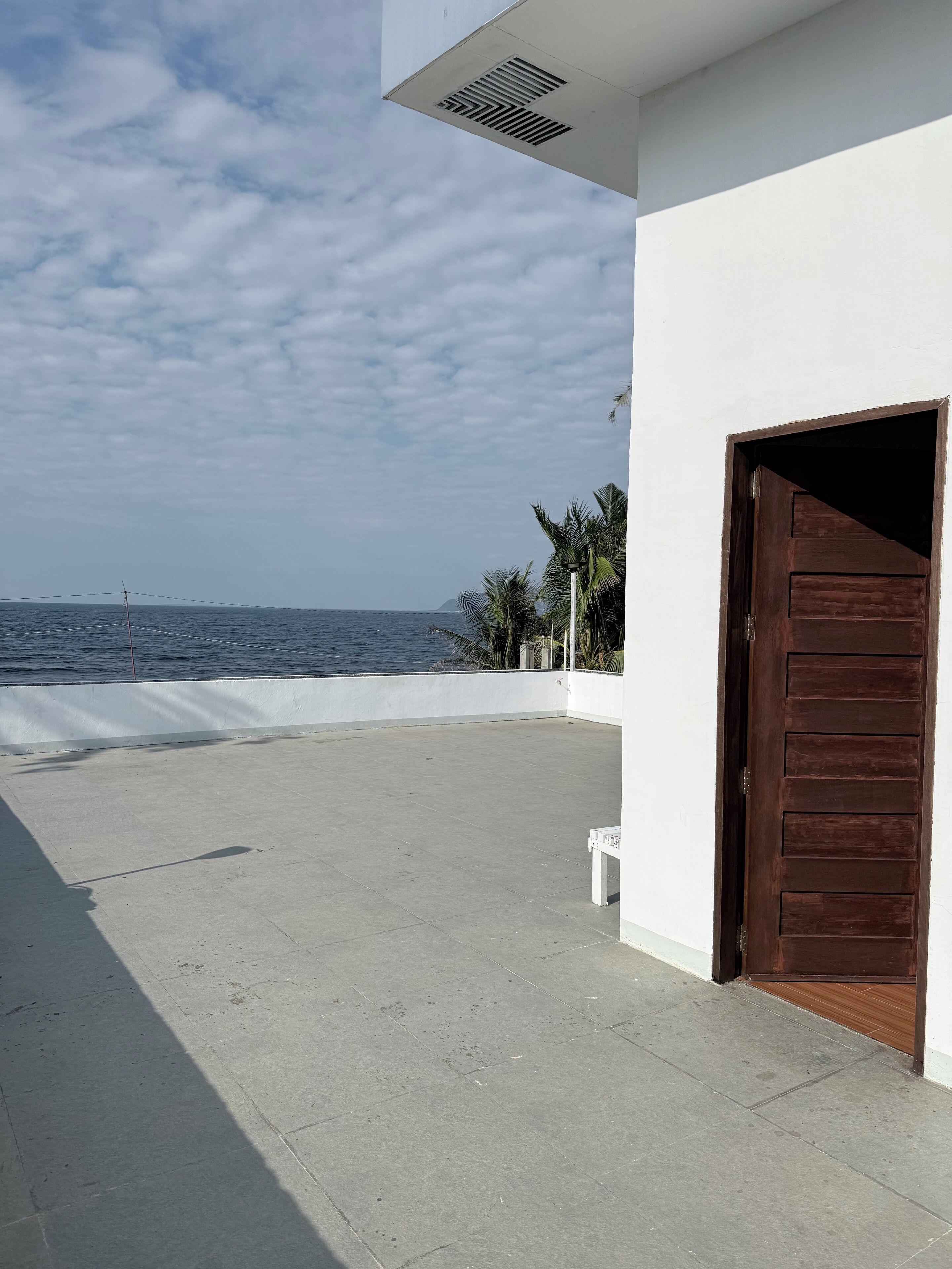 A building with a large open patio, a wooden door, and a view of the sea.