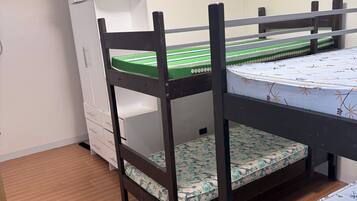 A bunk bed with a wooden frame and green mattress, a white wardrobe, and a white cabinet.