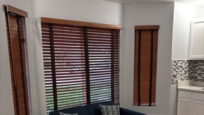 Ein Wohnzimmer mit einem dunkelblauen Sofa, zwei gemusterten Kissen und Holzjalousien an den Fenstern.