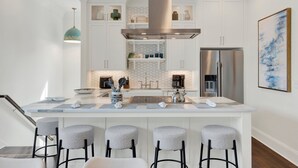Een moderne keuken met een centraal eiland, barkrukken, roestvrijstalen apparatuur en een decoratieve hanglamp.