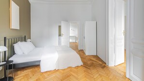 A bedroom with a bed, bedside table, and a mirror. There is a hallway leading to another room. - Blueground | Alsergrund, view, nr Votivkirche (Vienna)