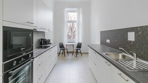 A modern kitchen with white cabinetry, a black oven, a granite countertop, and a window with a view of bare trees. - Blueground | Alsergrund, view, nr Votivkirche (Vienna)