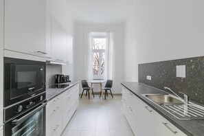 A modern kitchen with white cabinetry, a black oven, a granite countertop, and a window with a view of bare trees. - Blueground | Alsergrund, view, nr Votivkirche (Vienna)