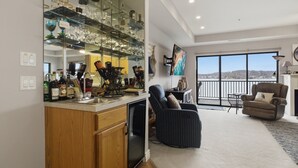 Ein modernes Wohnzimmer mit großem Fenster, einem Essbereich mit Glastisch und einer Küche mit Einbaukühlschrank.