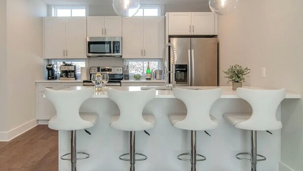 Une cuisine moderne avec des meubles blancs, des appareils en acier inoxydable et un îlot central doté de tabourets de bar.