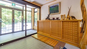 A reception area with a sliding glass door, a wooden reception desk, a framed painting, and a small wooden sculpture. - Onsen Oyado Ruribitaki (Matsumoto)