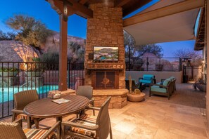 A patio with a stone fireplace, outdoor seating, and a pool view.