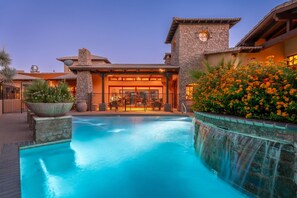 A pool with a waterfall feature, stone architecture, and a patio area.