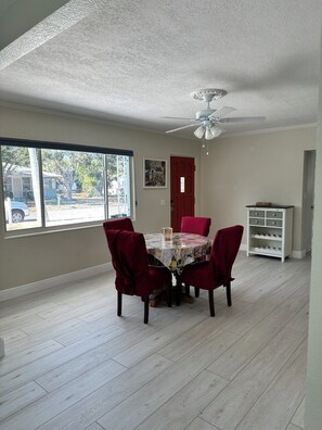 A dining area with a table and chairs, a ceiling fan, a window with a view of the street, and a door. - 3BR Coastal Getaway with Large Yard & BBQ near Anna Maria Island (Bradenton)