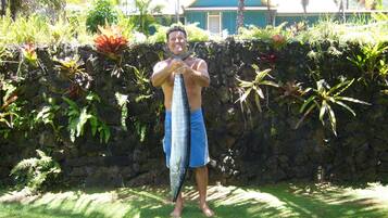 A person holding a large fish in front of a stone wall with tropical plants.