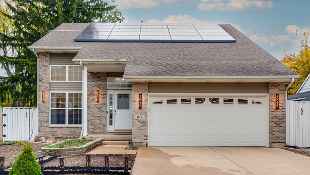 A two-story house with a garage, solar panels on the roof, and a brick exterior.