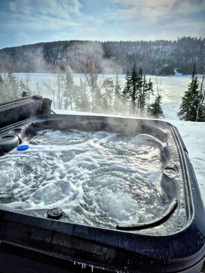 Ett bubbelbad med utsikt över ett snötäckt landskap och träd.