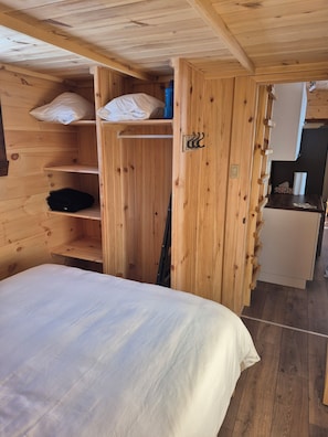 A wooden cabin interior with a bed, shelves, and a small kitchenette.