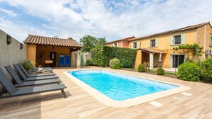A swimming pool with lounge chairs, a tiled deck, and a building with a tiled roof and shutters. - le gîte jaune des gîtes de Bel-Air en Luberon (TAILLADES)