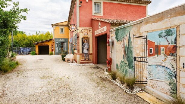 A building with a red facade, a mural on the right side, and a sign for 'SALALSONS' on the left. - The red gîte of the Gîtes de Bel-Air in Luberon (TAILLADES)