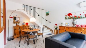 A modern living room with a black leather sofa, a wooden dining table with chairs, a staircase with a metal railing, and a cabinet with a 'ROUG' sign. - The red gîte of the Gîtes de Bel-Air in Luberon (TAILLADES)