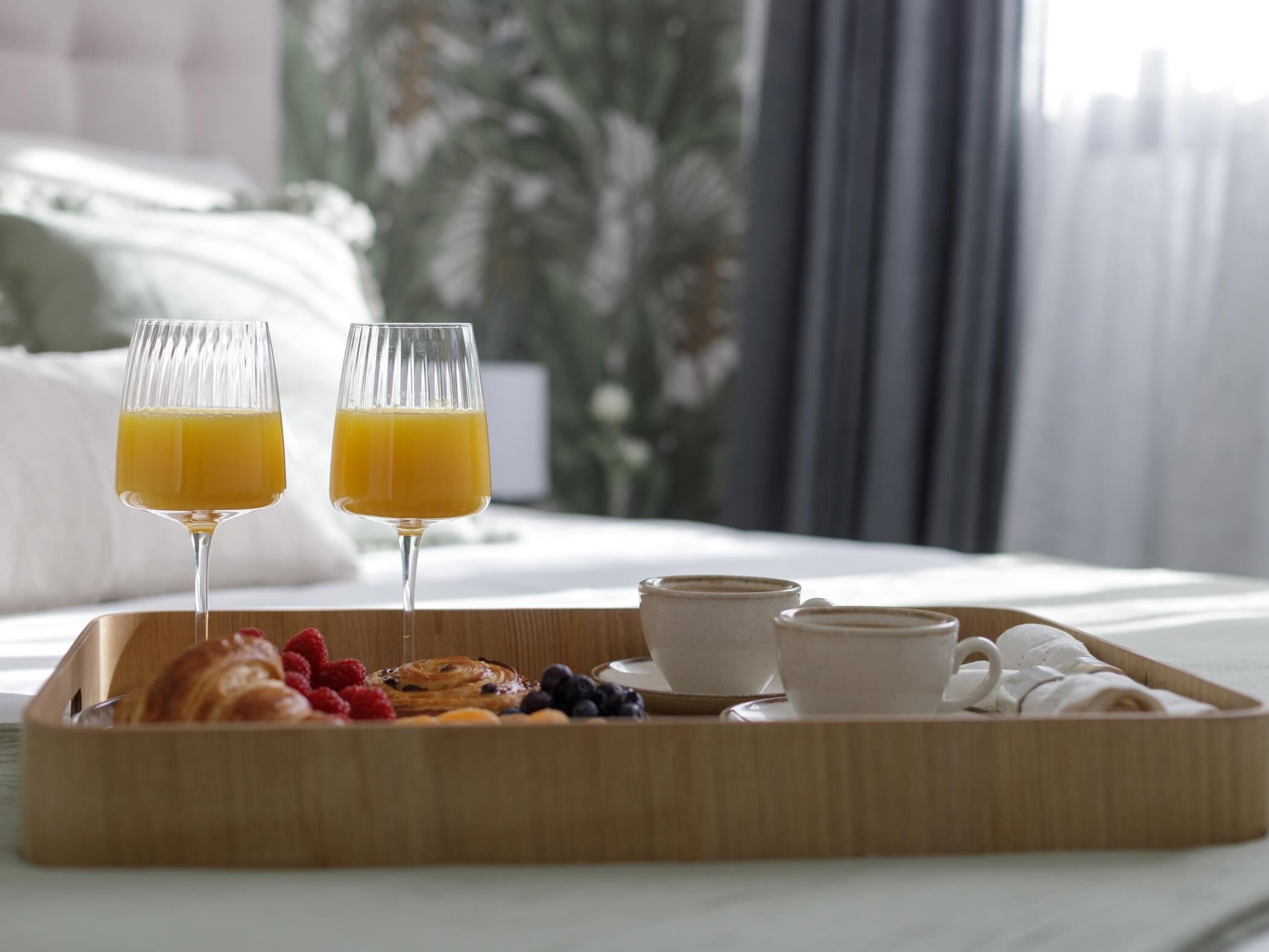 A breakfast tray with croissants, berries, and two glasses of orange juice on a bed.