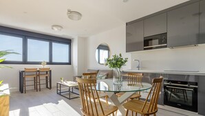 Una cucina moderna con forno integrato, un'area pranzo con tavolo in vetro e sedie in legno, e un'ampia finestra che offre luce naturale.