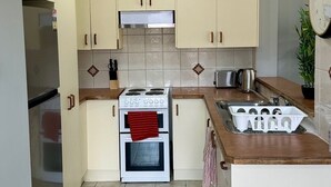 A modern kitchen with white cabinets, a gas stove, a built-in oven, a refrigerator, and a clock on the wall. - Home Away from Home (Liverpool)