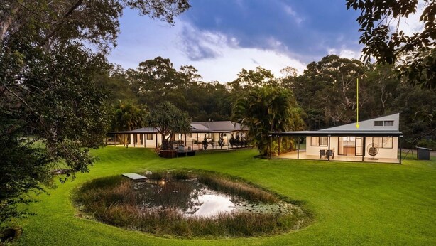 A modern house with a pond, surrounded by lush greenery and trees.