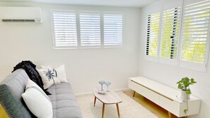 A modern living room with a grey sofa, white cushions, a wooden coffee table, a white bench, and a potted plant.