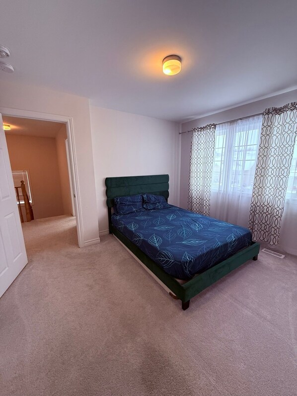 A bedroom with a bed, a door, a window with patterned curtains, and a ceiling light.