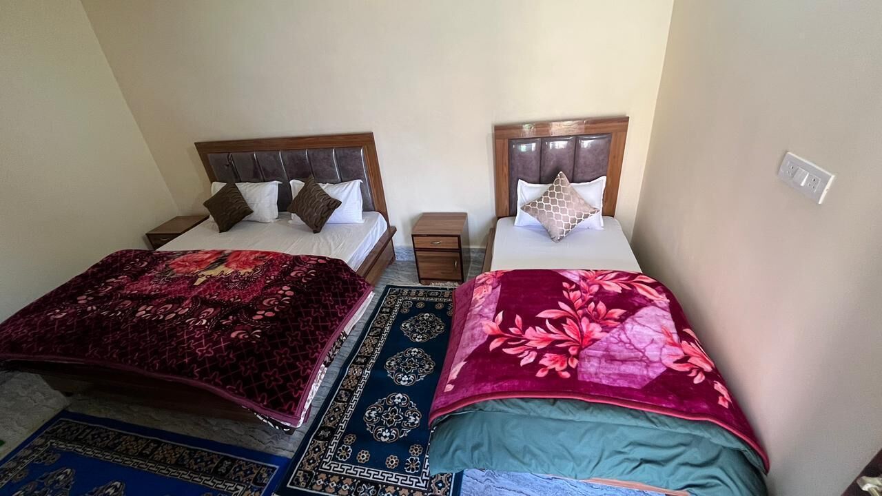 Una habitación con dos camas, cada una con cabecero de madera y una mesita de noche. Las camas están cubiertas con colchas estampadas.