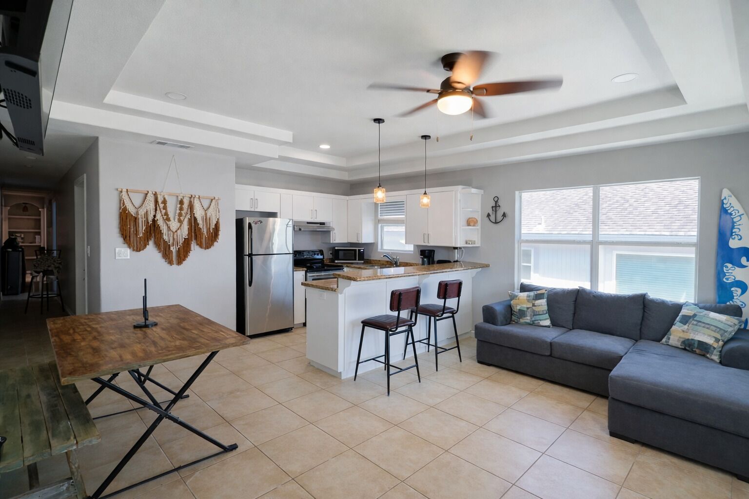 A modern kitchen with a central island, bar stools, a grey sofa, and a ceiling fan.