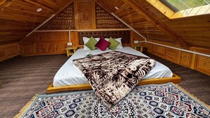 A cozy attic bedroom with a wooden ceiling, a large bed with patterned bedding, and a view of greenery through a skylight. - Mountain pine majesty jibhi  (Banjar)