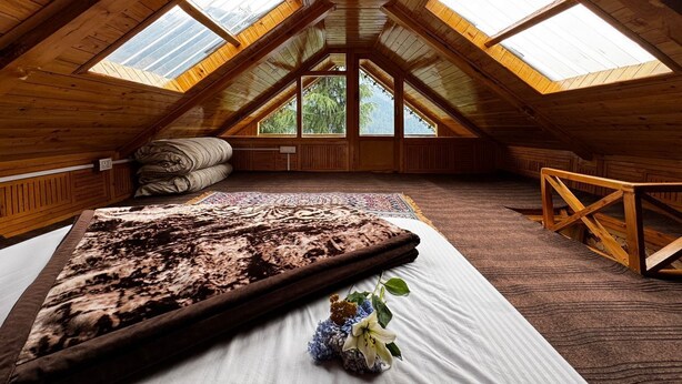 A high-ceilinged attic bedroom with skylights, a bed with a patterned bedspread, and a wooden bench. - Mountain pine majesty jibhi  (Banjar)
