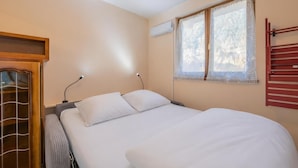 Een slaapkamer met een bed, een raam met kantgordijnen, een airconditioning en een houten garderobe.