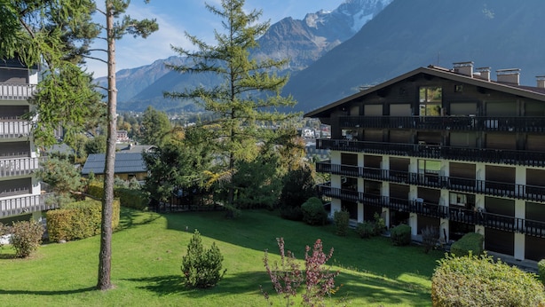 Et hotel med flere balkoner, en velholdt græsplæne og et bjerg i baggrunden.