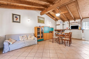 Ein gemütliches Wohnzimmer mit einem gestreiften Sofa, einem Esstisch mit Stühlen, einem Holzschrank und einer Küchenzeile inklusive Herd und einer Uhr.
